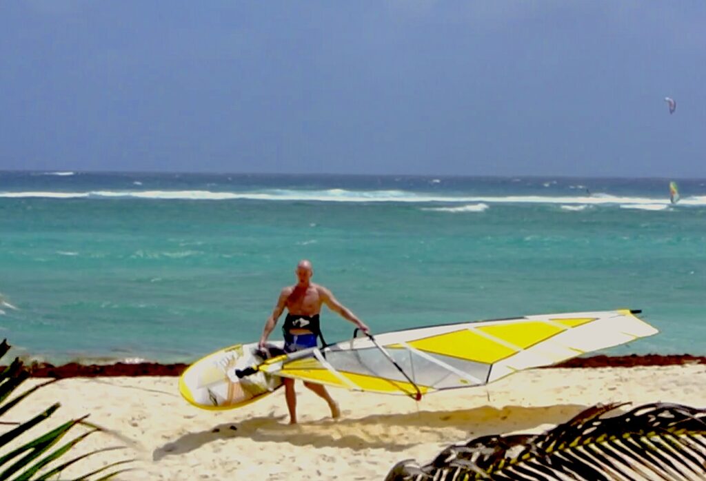 avid windsurfer carrying board and sail against the wind- one time when you may not be searching for the wind