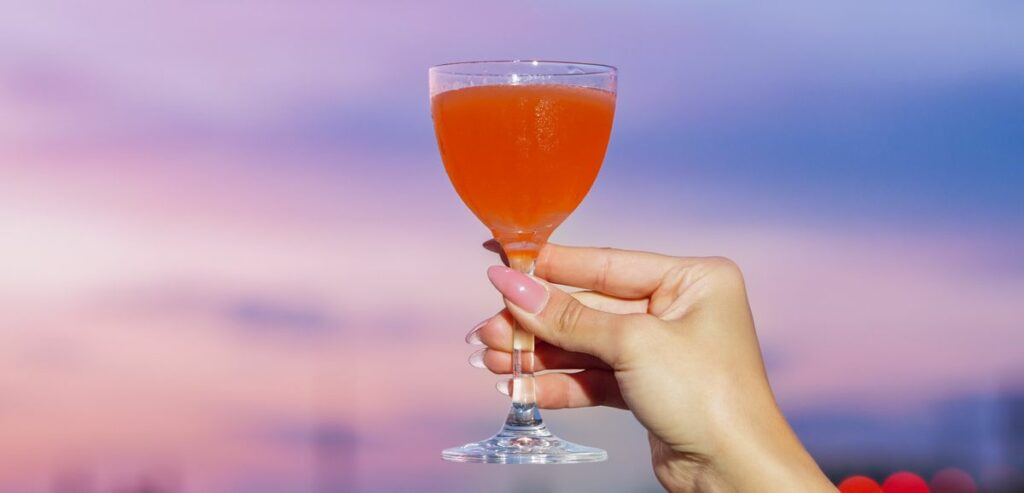 Lady holding tropical cocktail with colorful sunset in the background