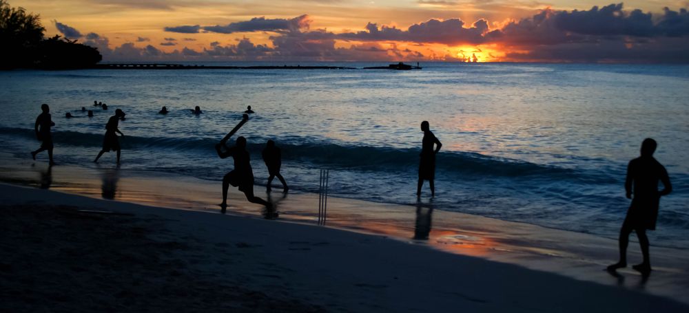 Group of men and boys playing beach cricket in Barbados at sunset