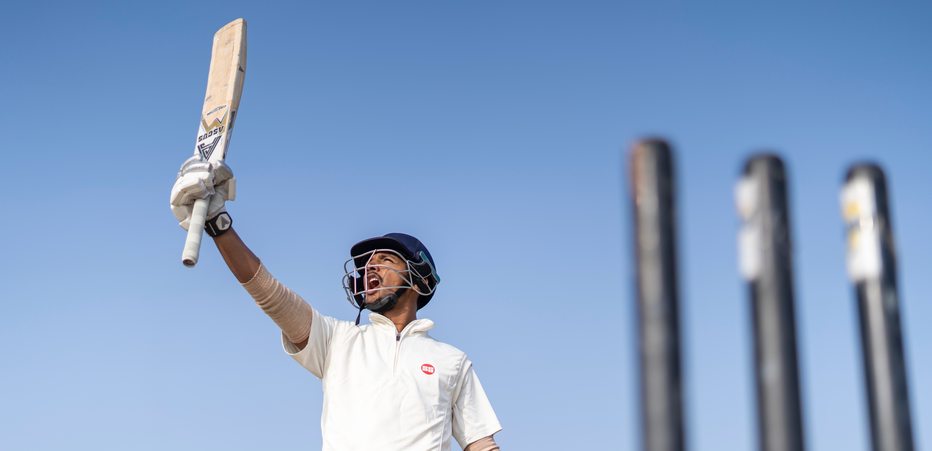 Cricketer holding a bat in victory.