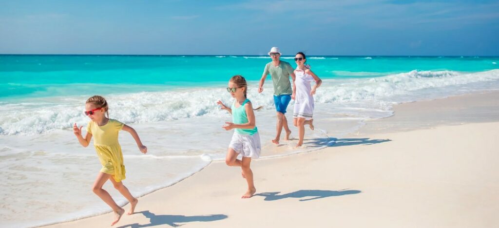 Family with 2 young girls walking on the beach backed by turquoise waters.