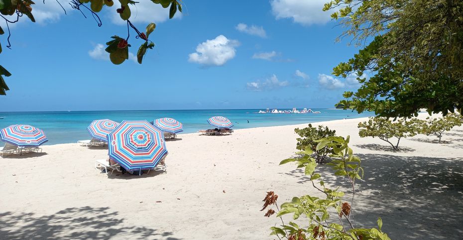 Beach scene on tranquil west coast of Barbados with blue skies, turquoise seas and colorful beach umbrellas.
