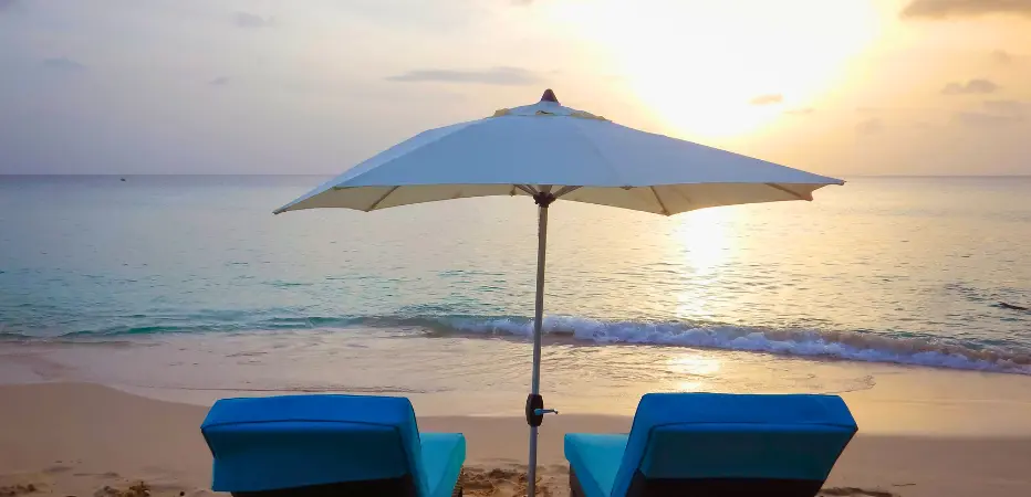 Two beach loungers under a beach umbrella looking onto calm waters and sunset on Barbados' west coast