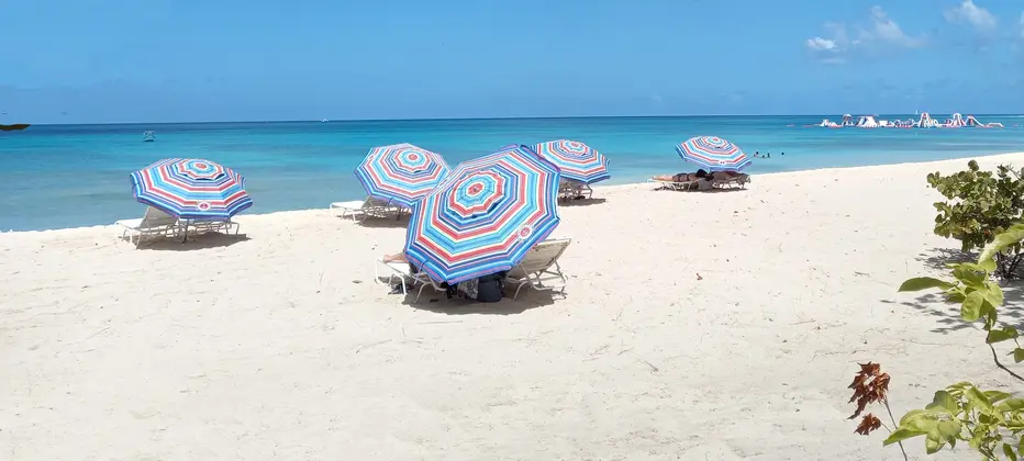 Colorful beach umbrellas and loungers sit on soft sands by tranquil turquoise shores