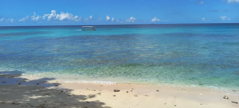 Coral reefs lie close to shore while a water taxi sails by further offshore